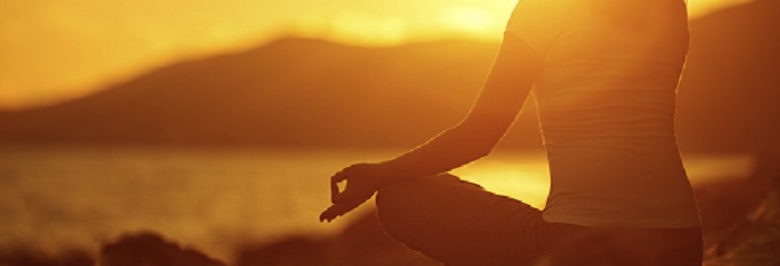 woman meditating in lotus pose on the beach at sunset